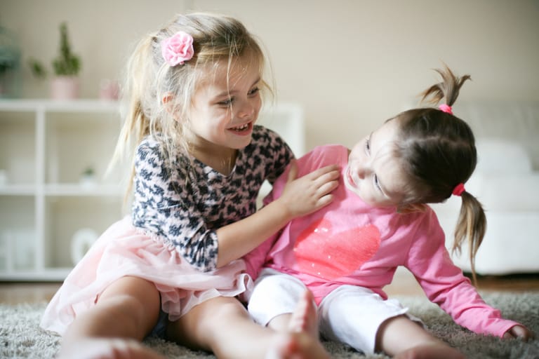 Kaksi tyttölasta leikkii kotona lattialla.