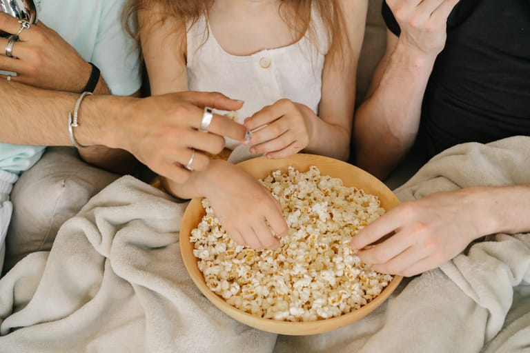 Kolmen henkilön kädet popcorn-kulhossa.