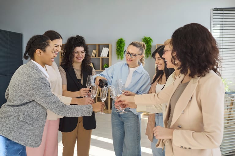 7 naista juomassa kuohuviiniä toimistolla.