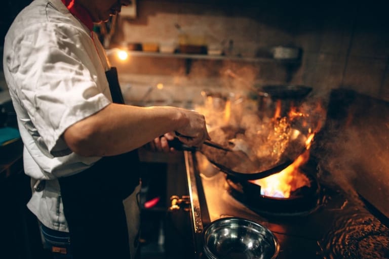 Ammattikokki paistaa wokkipannulla avotulen äärellä savuisessa ravintolakeittiössä