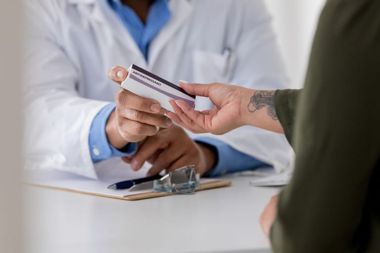 Lääkäri ojentaa masennuslääkepakkauksen potilaalle — Suomi on onnellisin maa mutta masennuslääkkeiden käyttö kaksinkertaistui