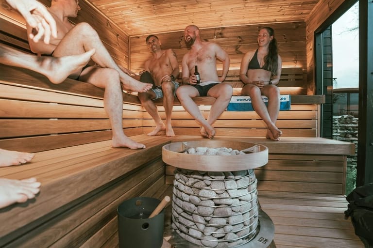 Ihmisiä saunomassa ja nauttimassa olutta kiukaan vierellä