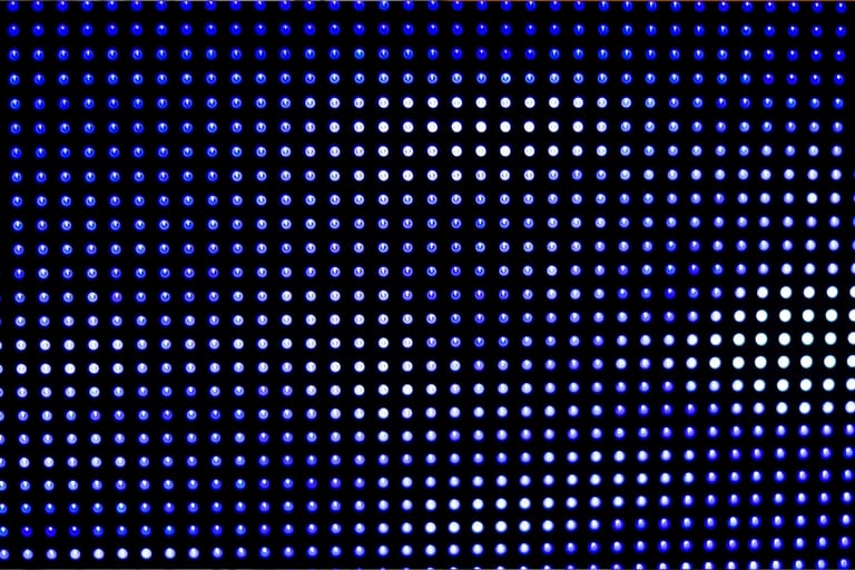 Lähikuva digitaalisesta näytöstä, jossa on tiheä ruudukko sinisiä ja valkoisia hohtavia pisteitä.