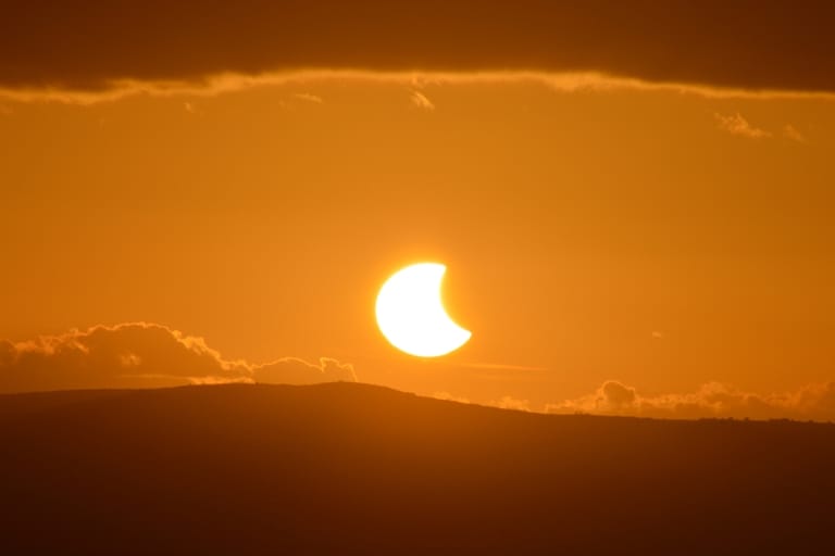 Oranssi osittainen auringonpimennys Suomen horisontissa, Kuu peittää suuren osan Auringosta.