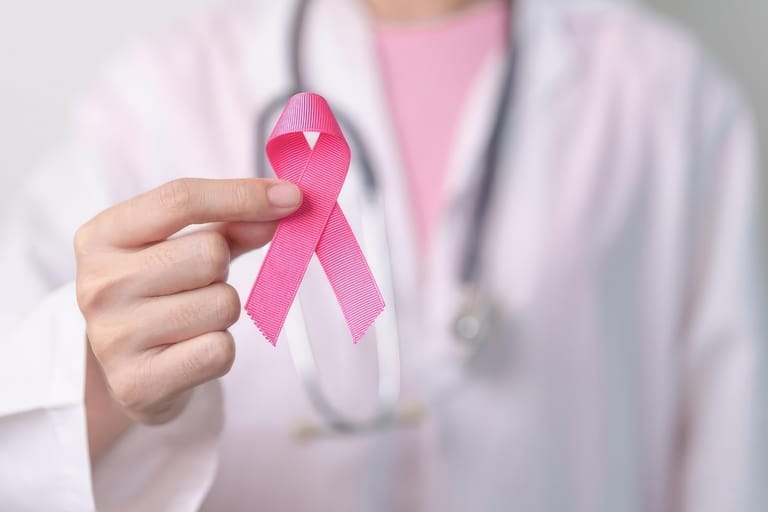Valkoista lääkärintakkia ja stetoskooppia käyttävä henkilö pitelee kädessään rintasyöpätietoisuuden vaaleanpunaista nauhaa.