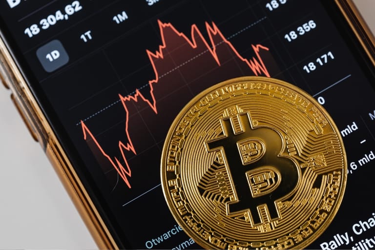 Bitcoin-kolikko älypuhelimen kryptokauppaa näyttävän kurssigraafin päällä.