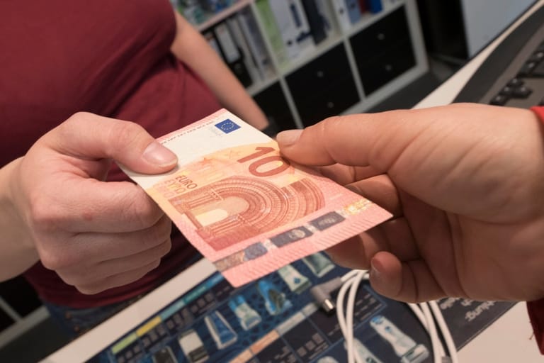 Kaksi ihmistä ojentaa toisilleen kymmenen euron seteliä.