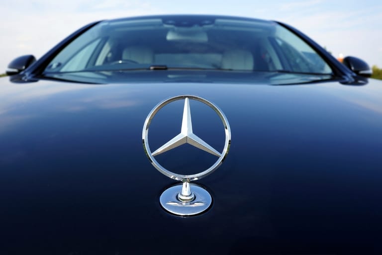 Hopeinen Mercedes-Benzin tähtitunnus tummansinisen henkilöauton konepellillä, auton tuulilasi taustalla.