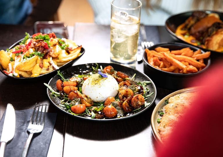 Ravintolapöydässä annoksia ja juomnia. Etualalla mozzarellaa ja tomaatteja.