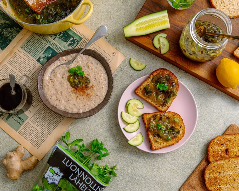 Pöydälle aseteltu aamiainen, jossa on puuroa, paahdettua leipää kurkkuhillolla sekä tuoreita vihanneksia ja yrttejä.