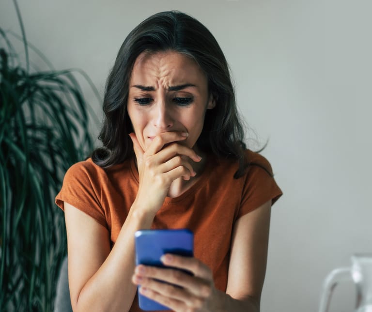 Nainen katsoo itkuisena puhelinta.