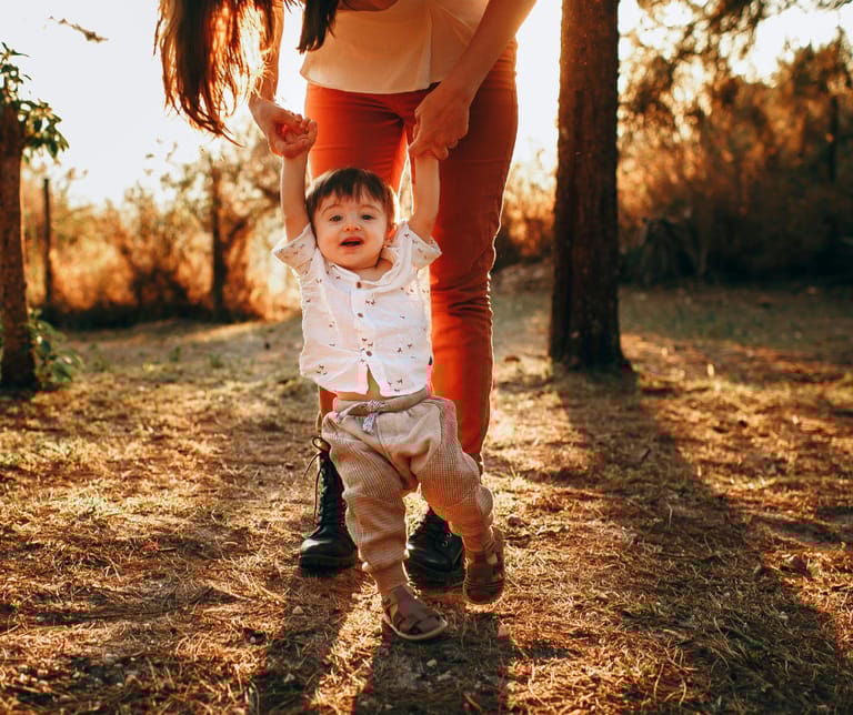 Äiti taluttaa taaperoa ilta.auringossa.