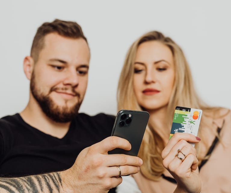Kuvassa mies ja nainen. Miehellä on kädessä kännykkä ja naisella pankkikortti.