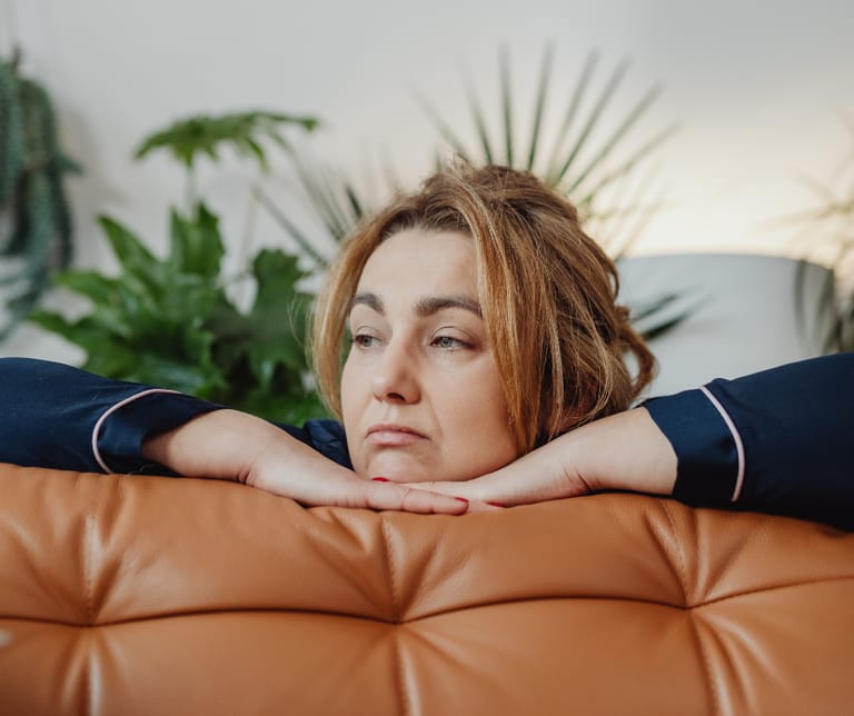 Kuvassa tyytymätön nainen nojaa oranssin nahkasohvan selustaan.
