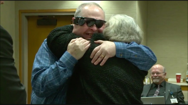 Allen Zderad syleilee vaimoaan bioniset silmälasit päässään.