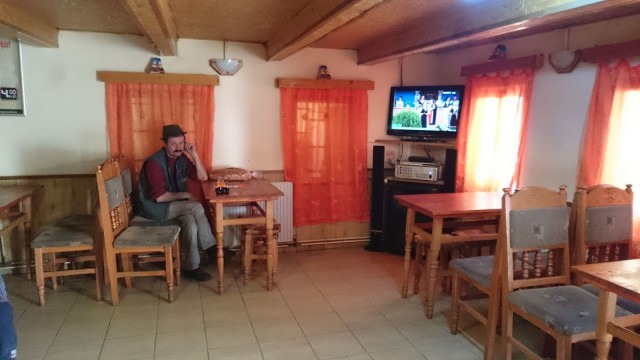 Romanialainen istuskelee kahvilassa. Televisiosta tulee paikallista musiikkia.