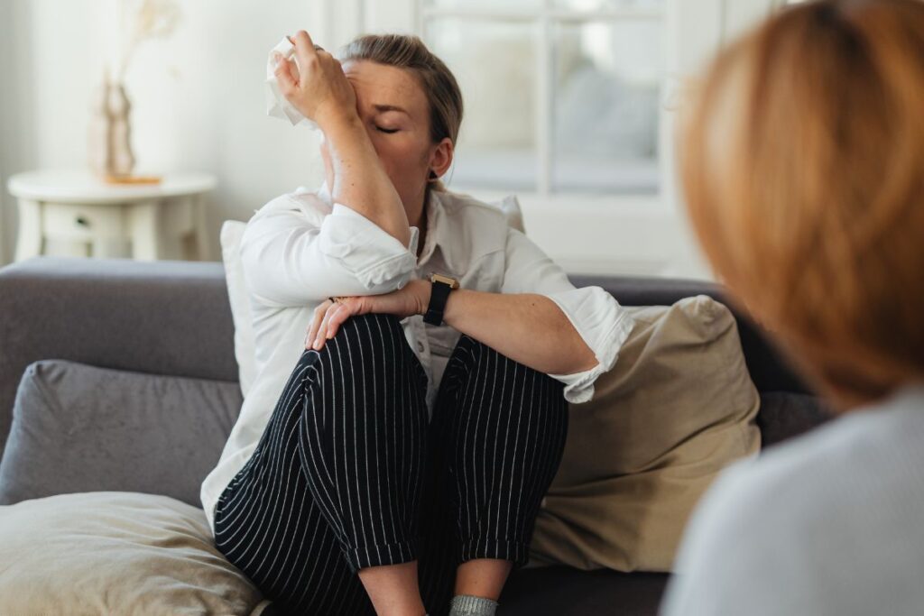 Nainen itkee terapeutille ja istuu vastapäätä sohvalla, pyyhkii nenäänsä