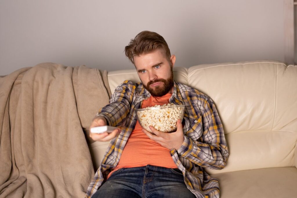 mies kaukosäädin ja popcornkulho katselee elokuvaa