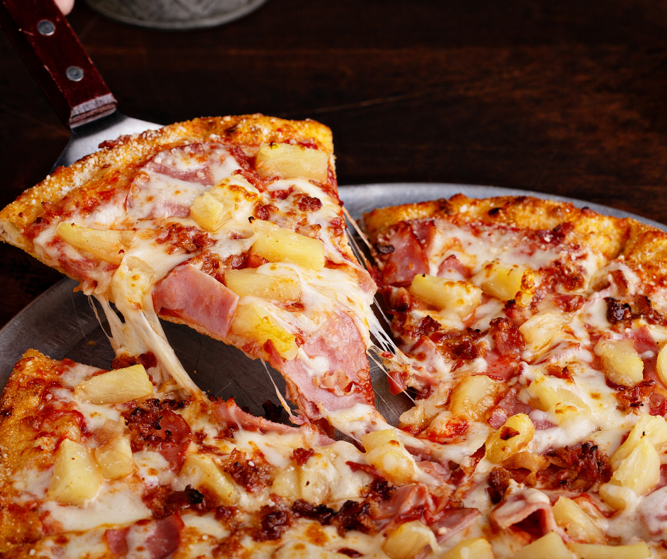 Kuvassa kinkku-ananaspizzaa, josta ollaan juuri ottamassa palaa.