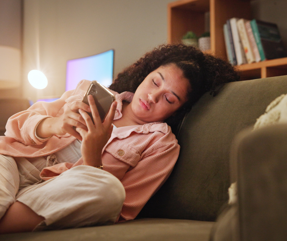 Kuvassa nainen lojuu väsyneenä sohvalla ja viestittelee kännykällä.