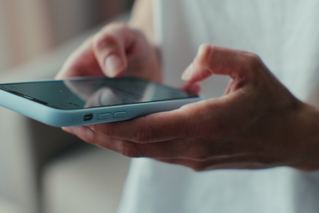 Lähikuva käsistä, jotka pitelevät vaaleansinistä älypuhelinta. Toisella kädellä henkilö selaa tai kirjoittaa viestiä kosketusnäytöllä. Kuva keskittyy puhelimen käyttöön ja viestintään, ja se sopii esimerkiksi someviestintään, deittailuun tai yhteydenpitoon liittyvään aiheeseen.