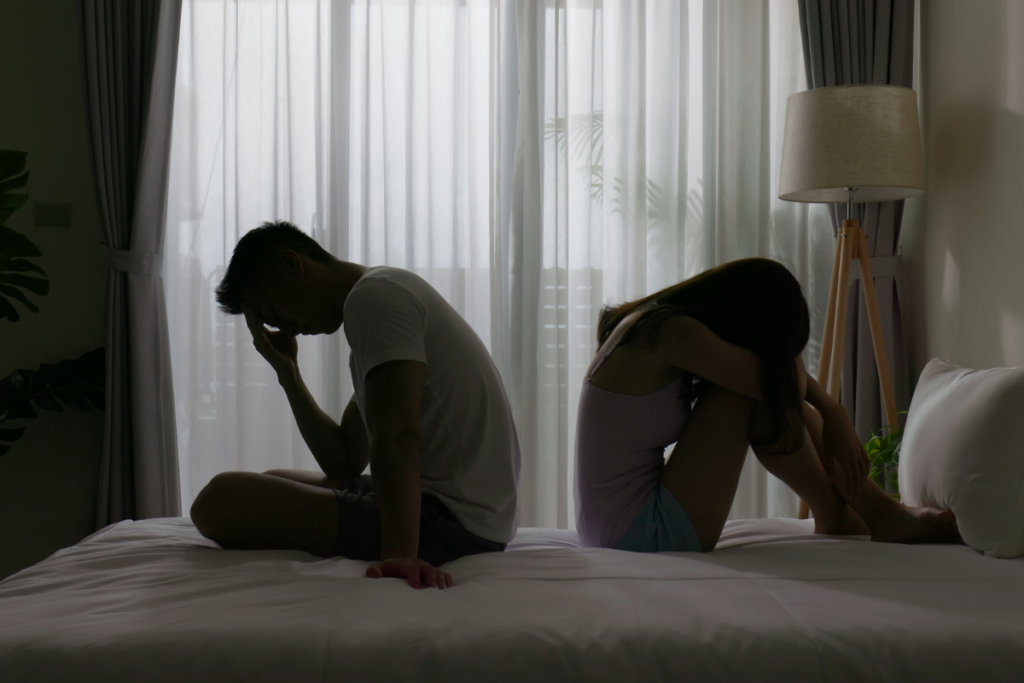 Kuvassa mies ja nainen istuvat sängyllä selät vastakkain ja nojaavat ominn käsiinsä. Molemmat ovat pettyneitä ja surullisia.