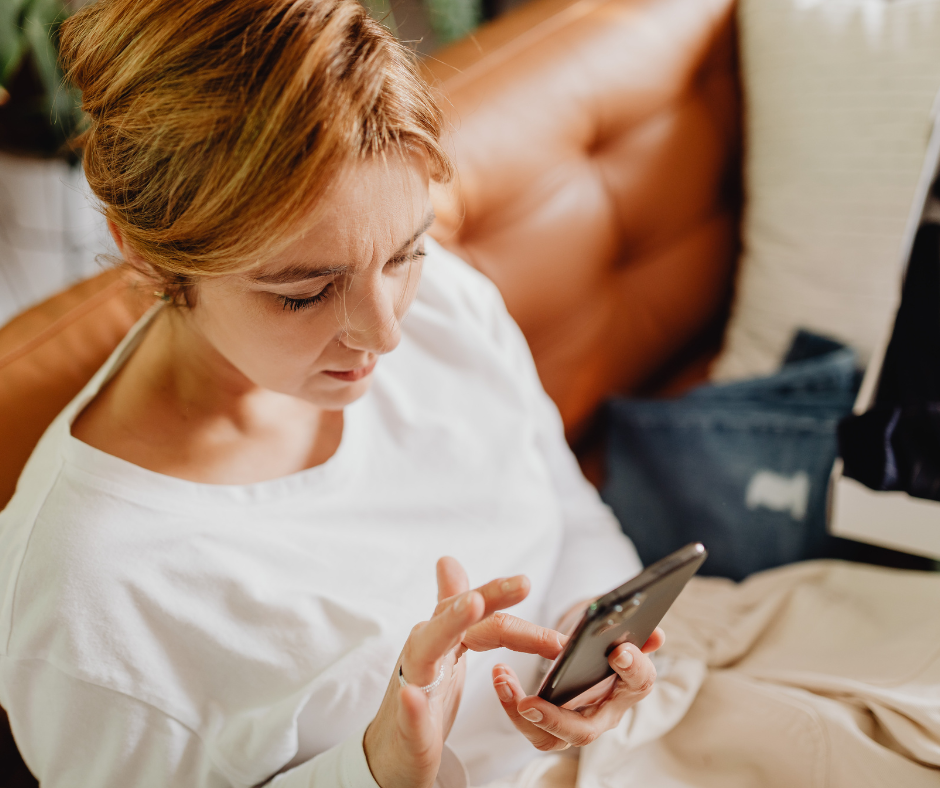 Nainen selaa puhelinta tyytymättömänä oranssilla sohvalla.