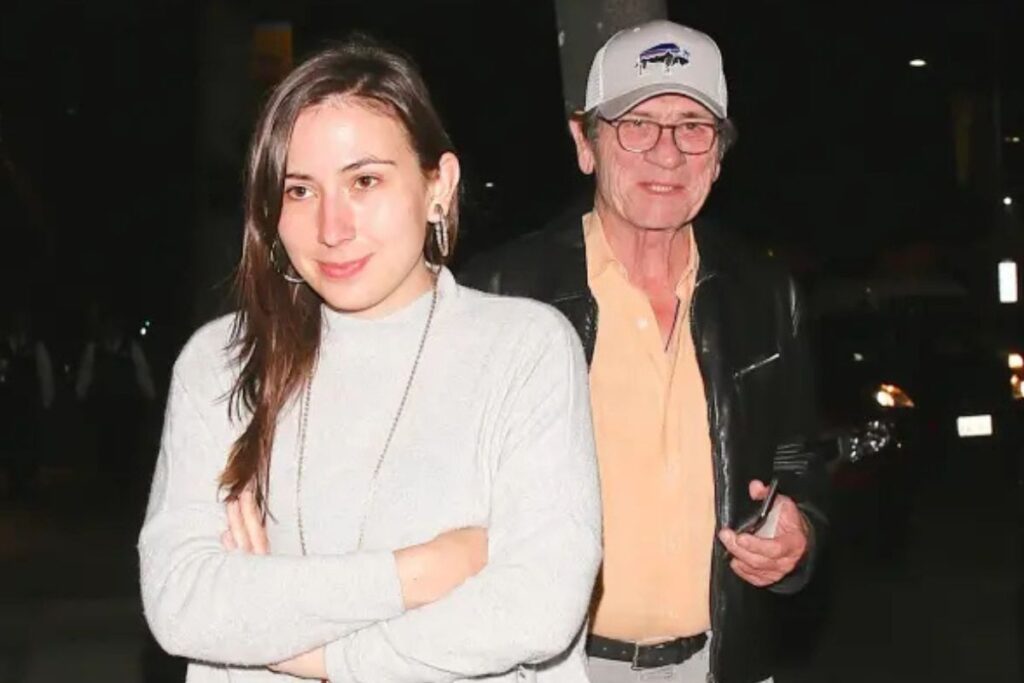 Paparazzikuva Tommy Lee Jonesista ja hänen tyttärestään Victoria Jonesista. He kävelevät kadulla ja näyttävät olevan hämmentyneitä kuvaamisesta. Kuvaaja on käyttänyt voimakasta salamavaloa, koska ulkona on pimeää.