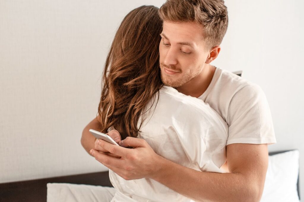 Nainen halaa miestä, mutta mies touhuaa täysin omiaan puhelimella epäluotettavan oloisena.
