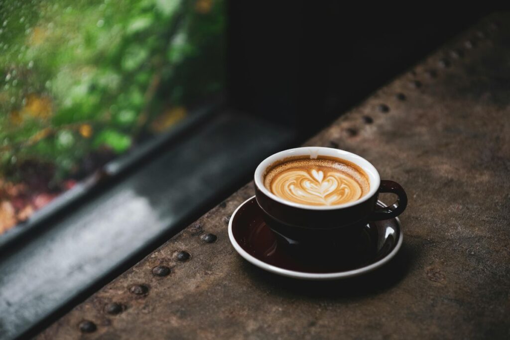 Kupillinen kahvia tummasävyisessä ympäristössä. Kahvin pinnalle on tehty maitovaahdolla kuvio. 