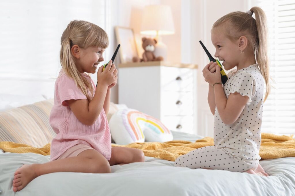 Kaksi pientä lasta istuu sängyllä vastakkain ja leikkii puhelimilla sisätiloissa.