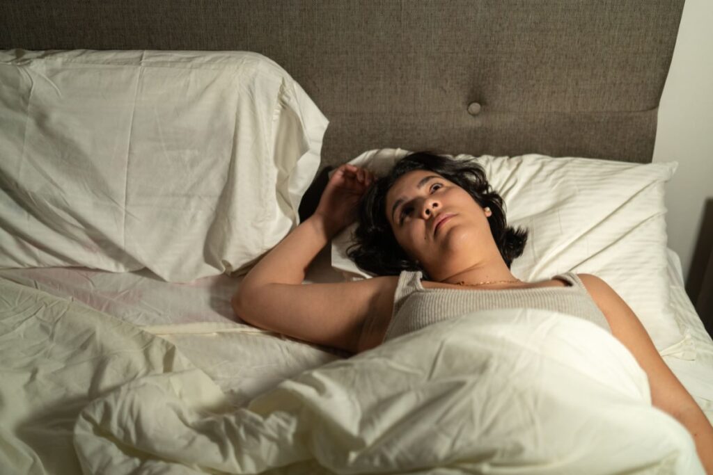 Nainen makaa hereillä sängyssä ja katsoo kattoon. 
