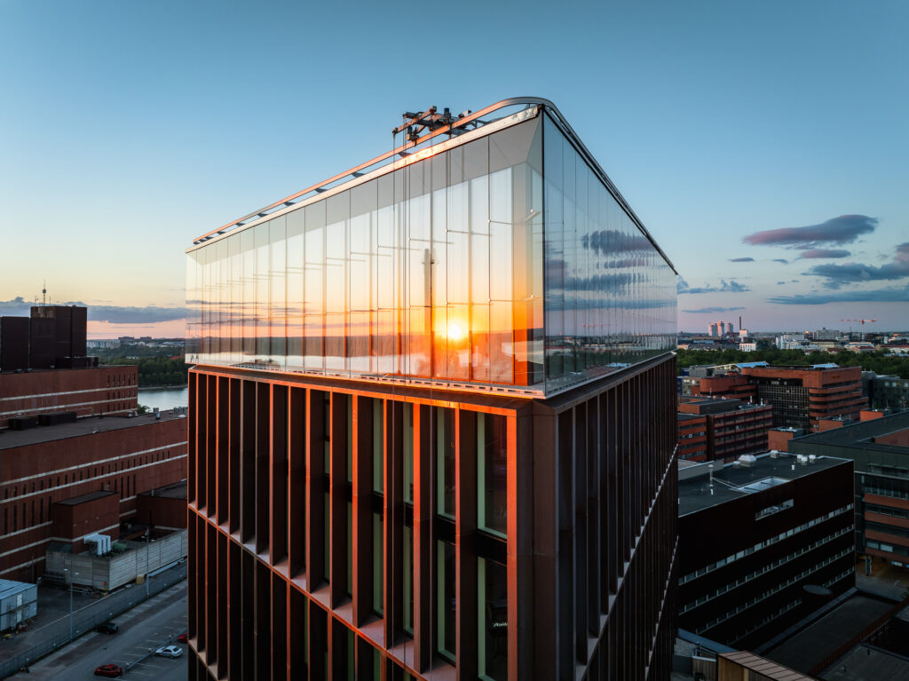 "Moderni lasinen toimistorakennus kaupunkimaisemassa auringonlaskun aikaan.
