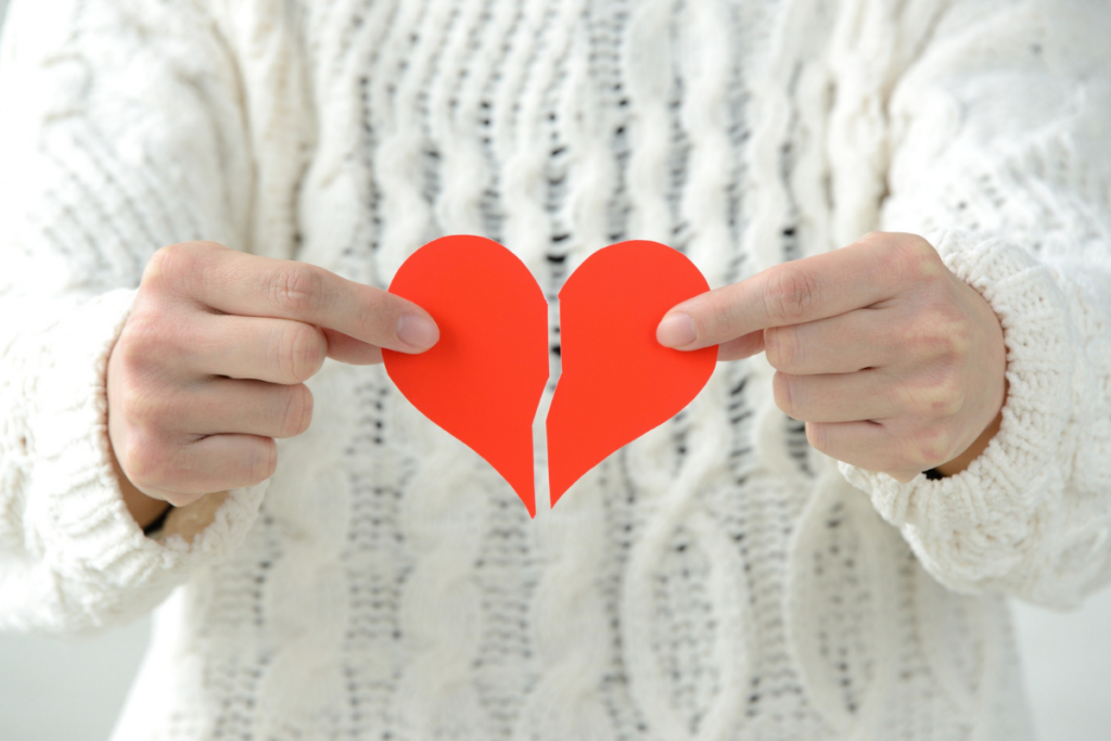 Henkilö pitelee käsissään kahtia revittyä punaista paperisydäntä vaaleaa neuletta vasten, mikä symboloi sydänsurua tai eroa.