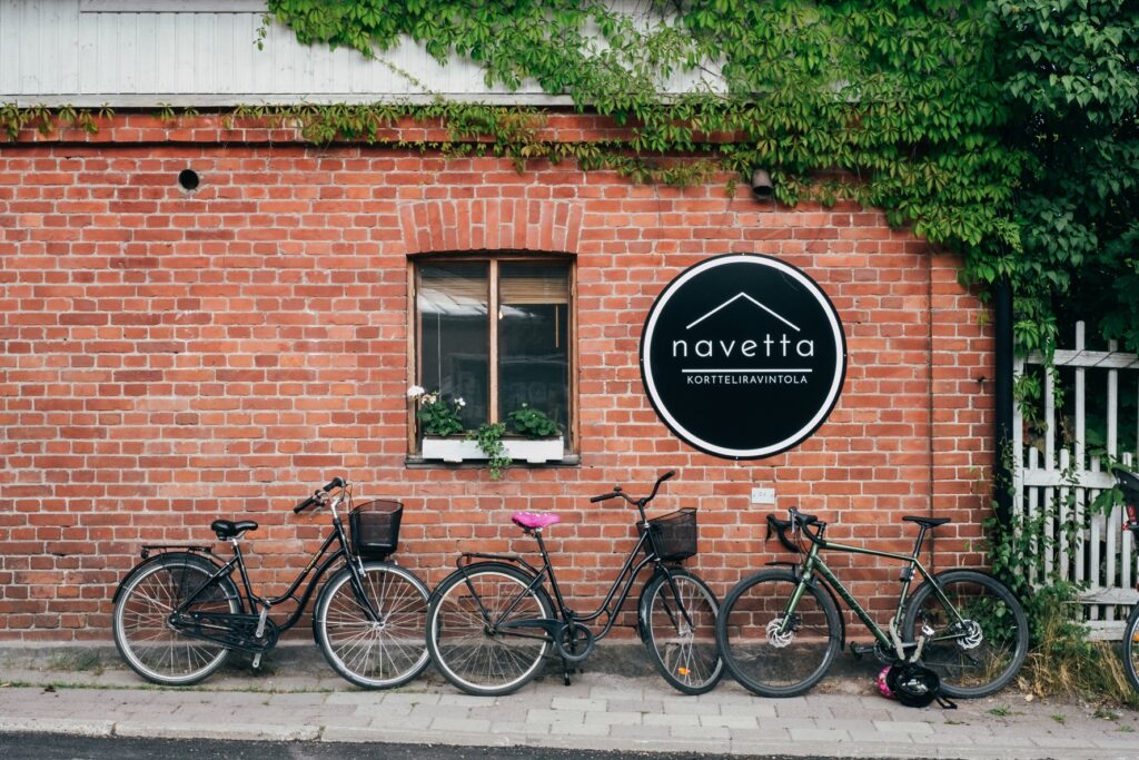Tiiliseinään kiinnitetty Navetta-kortteliravintolan pyöreä kyltti ja seinän vieressä pysäköityjä polkupyöriä.