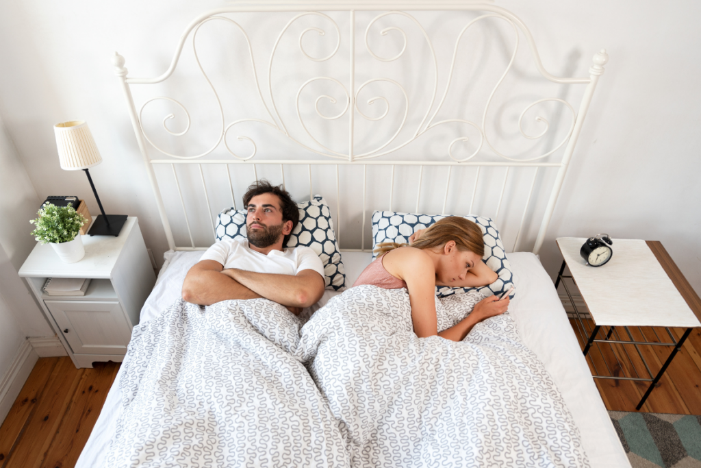 Pariskunta makaa sängyssä selät vastakkain, molemmat hereillä ja ajatuksiinsa uppoutuneina, tunnelma on etäinen ja ristiriitainen.