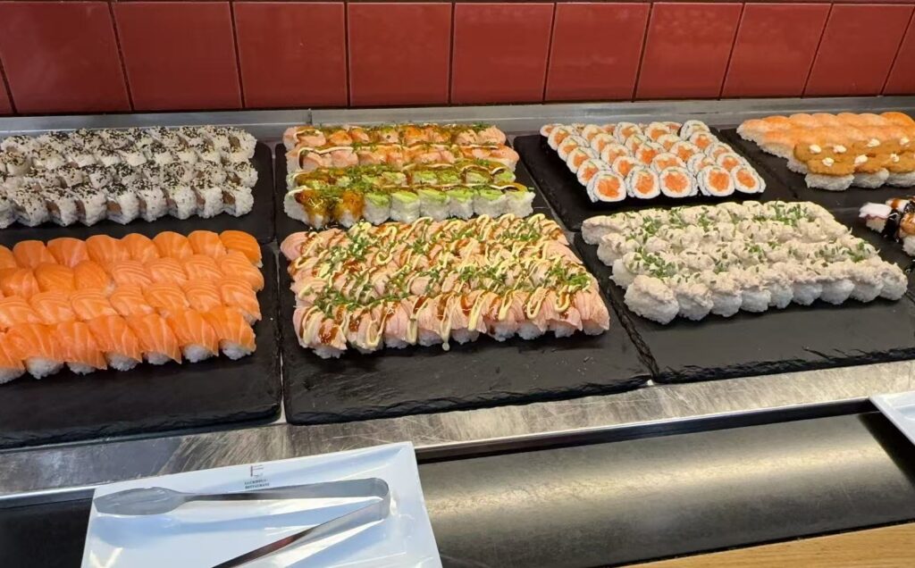 Sushibuffet, jossa esillä erilaisia sushirullia ja nigirejä, kuten lohinigiriä, makirullia ja erikoisrullia kastikkeilla, aseteltuna mustille kivitarjottimille.