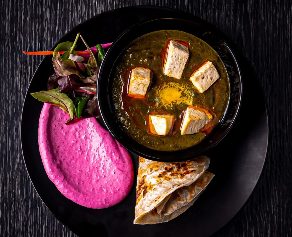 Kulhollinen vihreää curryä paneer-juustolla, tarjoiltuna naan-leivän ja punajuurihummuksen kanssa.