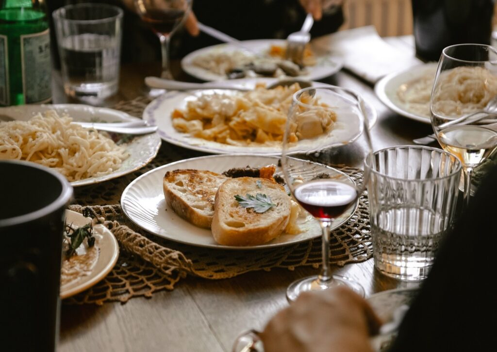 Ravintolapöytä, jossa useita pastaruokia, paahdettua leipää ja viinilaseja yhteisellä aterialla.