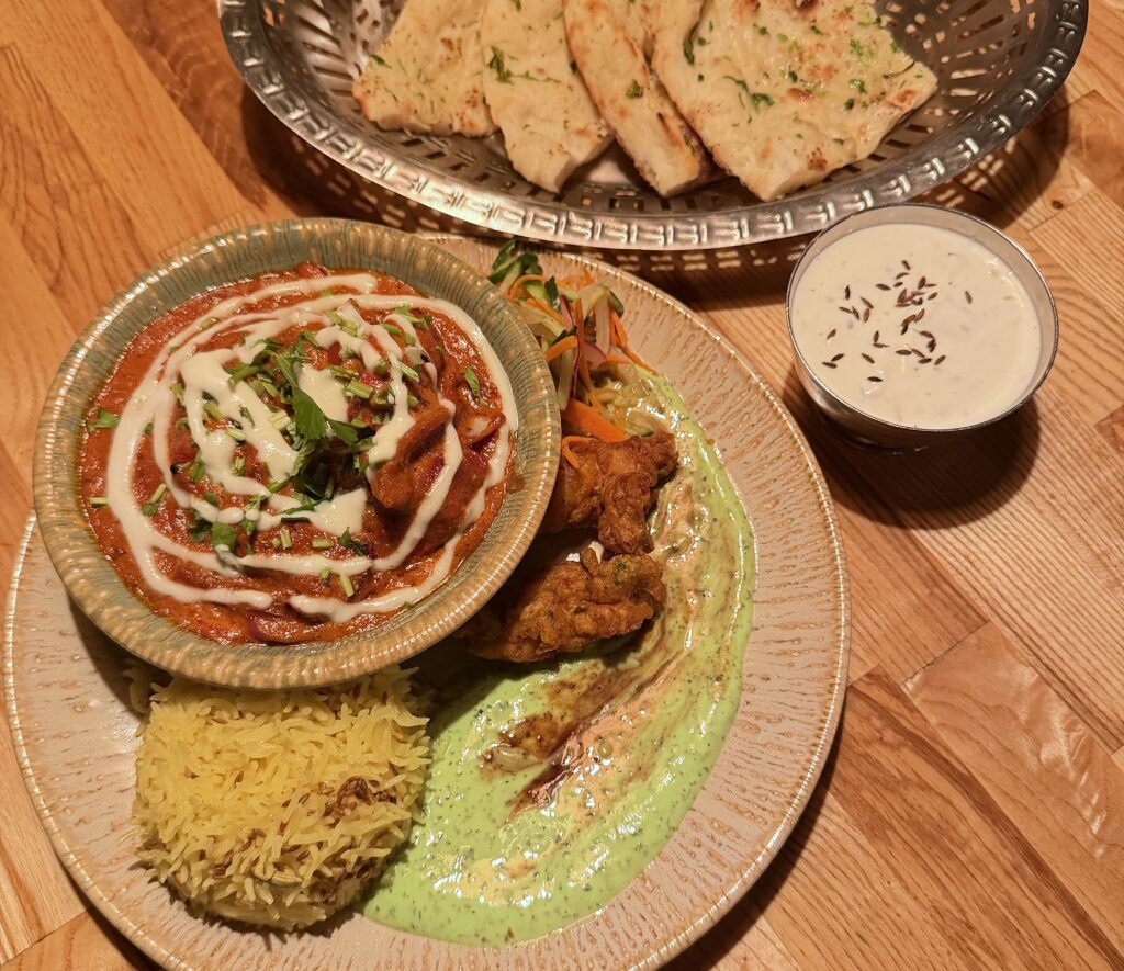 Intialainen ateria, jossa kulhollinen tomaattipohjaista curryä, basmatiriisiä, vihreää kastiketta ja naan-leipää.