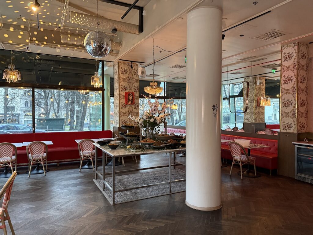 Tilava ravintolasali, jossa pitkät punaiset sohvat, koristeellinen sisustus ja keskellä kattauspöytä.