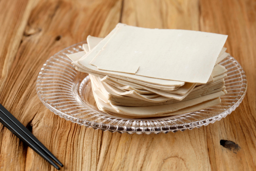 Pinottuja wonton- tai dumplingtaikinalevyjä lasilautasella puupöydällä.