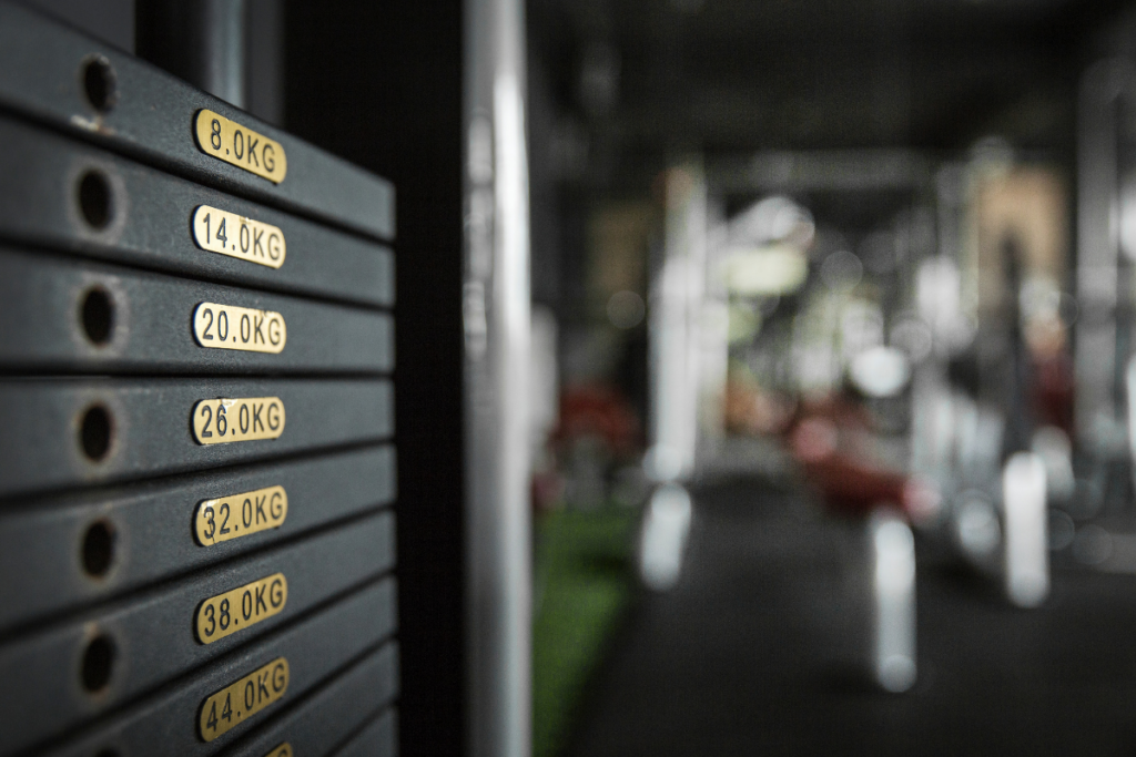 Kuntosalilaitteen painopakka, jossa näkyvät painomerkinnät 8–44 kilogrammaa, taustalla epätarkka saliympäristö.