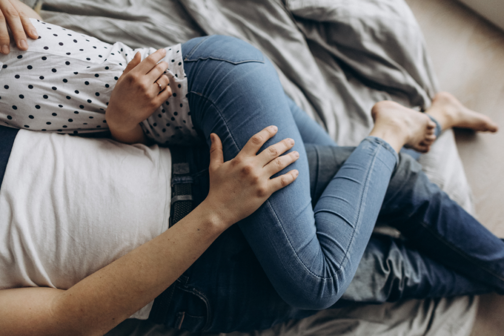 Kaksi aikuista makaa sängyssä kyljellään, toisen käsi lepää toisen reidellä