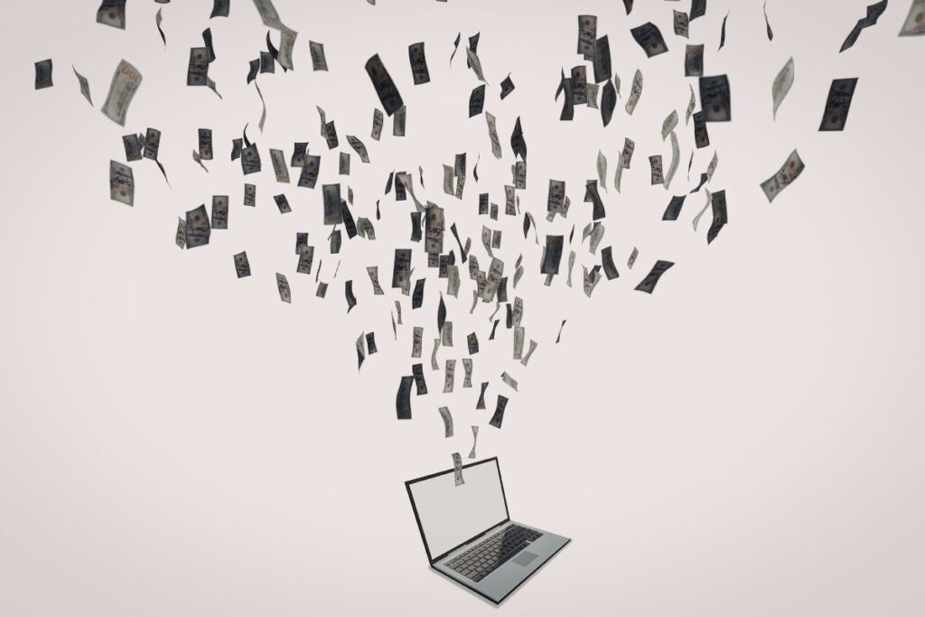 Kannettava tietokone, jonka yläpuolella leijuu ja putoilee seteleitä.