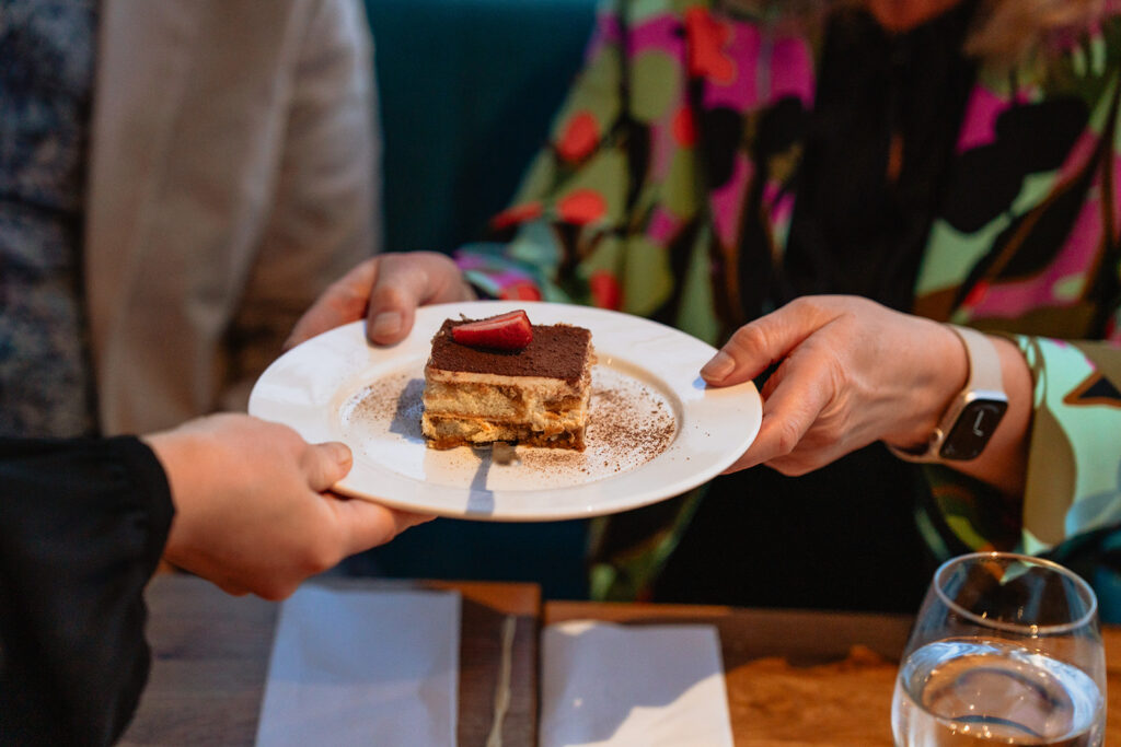Jälkiruoka-annos ojennetaan pöydässä: pala kerroksellista kakkua valkoisella lautasella.