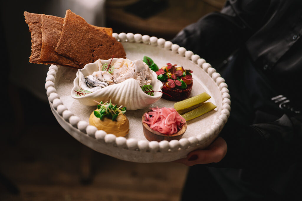 Tarjoilija pitelee tyylikästä alkuruokalautasta, jossa kalaa, lisukkeita ja leipää.