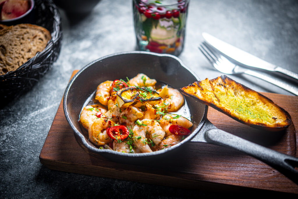 Katkarapuannos pannulla: paistettuja katkarapuja, chiliä ja yrttejä, vieressä paahdettua leipää.