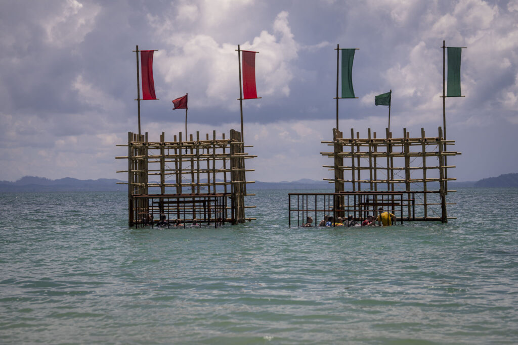 Kaksi puista rakennelmaa meressä, osallistujia häkkimäisissä rakenteissa kilpailutehtävän aikana.
