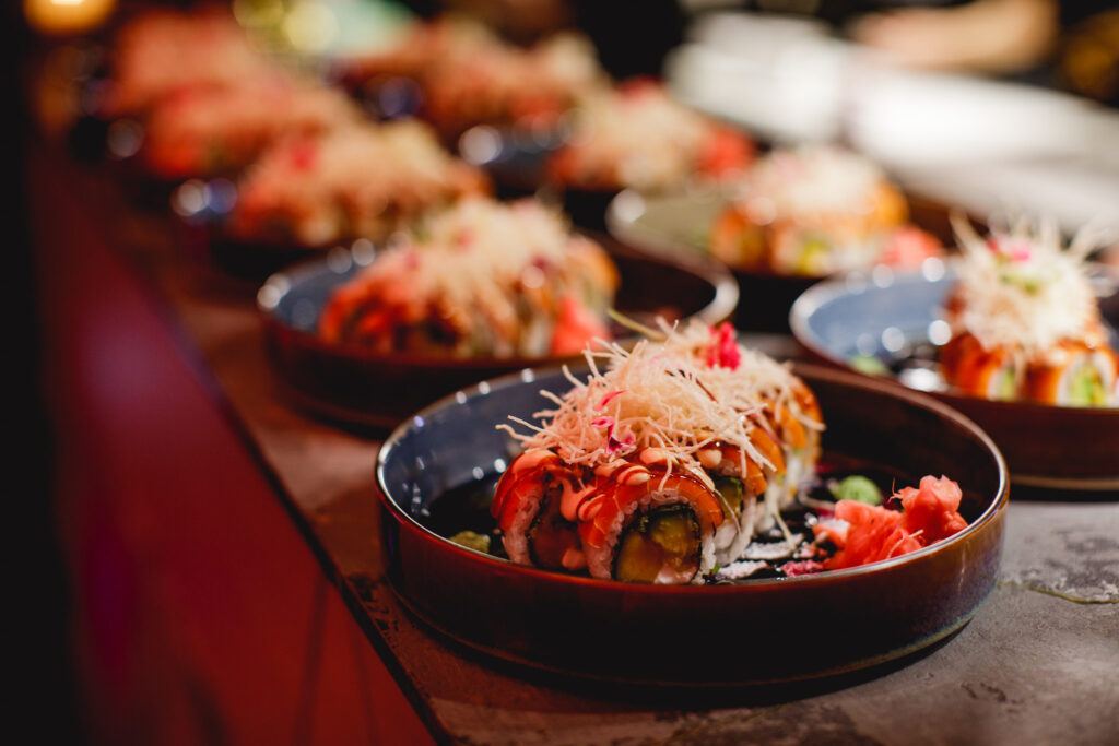 Sushiannoksia riveissä ravintolapöydällä, etualalla sushi rullana kulhossa.